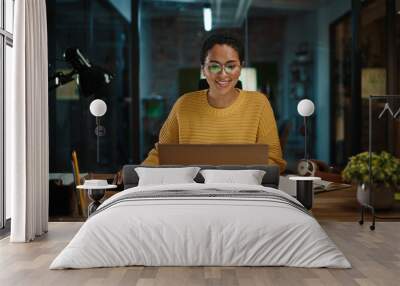 Portrait of Young Latina Marketing Specialist Working on Laptop Computer in Busy Creative Office Environment. Beautiful Diverse Multiethnic Female Project Manager is Browsing Internet. Wall mural