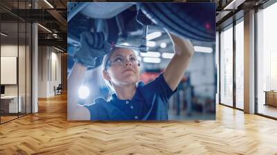 Portrait Shot of a Female Mechanic Working Under Vehicle in a Car Service. Empowering Woman Wearing Gloves and Using a Ratchet Underneath the Car. Modern Clean Workshop.  Wall mural