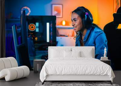 Pretty and Excited Black Gamer Girl in Headphones is Playing First-Person Shooter Online Video Game on Her Computer. Room and PC have Colorful Neon Led Lights. Cozy Evening at Home. Wall mural