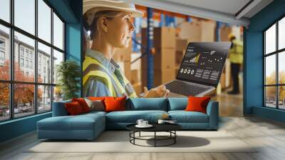 Professional Female Worker Wearing Hard Hat Holds Laptop Computer with Screen Showing Analysis Software in the Retail Warehouse full of Shelves with Goods. Over the Shoulder Side View  Wall mural