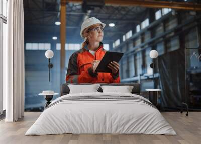 Professional Heavy Industry Engineer Worker Wearing Safety Uniform and Hard Hat, Using Tablet Computer. Serious Successful Female Industrial Specialist Walking in a Metal Manufacture Warehouse. Wall mural