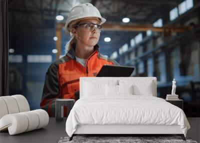 Professional Heavy Industry Engineer/Worker Wearing Safety Uniform and Hard Hat Uses Tablet Computer. Serious Successful Female Industrial Specialist Walking in a Metal Manufacture Warehouse. Wall mural