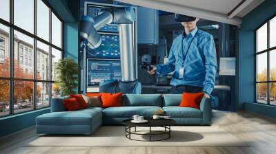 Professional Japanese Development Engineer in Blue Shirt is Controlling a Futuristic Robotic Arm with a Virtual Reality Headset and Joysticks in a High Tech Research Laboratory with Modern Equipment. Wall mural