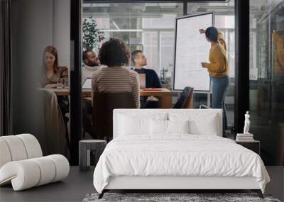 Project Manager Makes a Presentation for a Young Diverse Creative Team in Meeting Room in an Agency. Colleagues Sit Behind Conference Table and Discuss Business Development, User Interface and Design. Wall mural