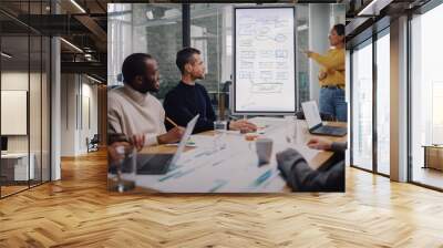 Project Manager Makes a Presentation for a Young Diverse Creative Team in Meeting Room in an Agency. Colleagues Sit Behind Conference Table and Discuss Business Development, User Interface and Design. Wall mural