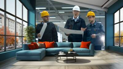 senior engineer and two workers are walking with papers through the factory space. Wall mural