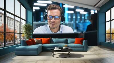 Serious Young Caucasian Man with Headset, Successful Manager of Call Center Sits in Office, Uses Computer, Talking on Video Conference with Client or Employee. Helpline Concept Wall mural