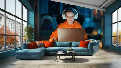 Smart Young Boy in Headphones Using Laptop Computer in Cozy Dark Room at Home. Happy Teenager Browsing Educational Research Online, Chatting with Friends, Studying School Homework. Wall mural