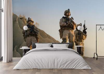 Squad of Three Fully Equipped and Armed Soldiers Standing on Hill in Desert Environment in Sunset Light. Wall mural