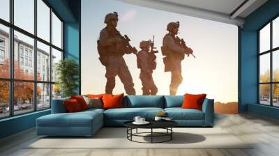 Squad of Three Fully Equipped and Armed Soldiers Standing on Hill in Desert Environment in Sunset Light. Wall mural