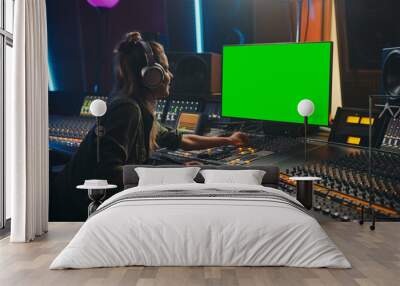 Stylish Female Audio Engineer / Producer Working in Music Record Studio, Uses Headphones, Green Screen Computer Display, Mixer Board, Control Desk to Create New Song. Creative Artist Musician. Wall mural