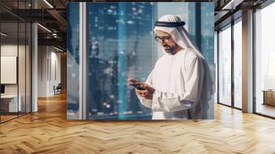 Successful Muslim Businessman in Traditional White Outfit Standing in His Modern Office, Using Smartphone Next to Window with Skyscrapers. Successful Saudi, Emirati, Arab Businessman Concept. Wall mural