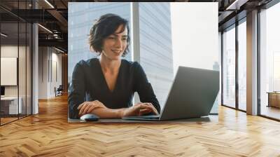 Successful Smiling Businesswoman Working on a Laptop in Her Modern Office. Stylish Beautiful Woman Doing Important Job. In the Window Big City Business District View.  Wall mural