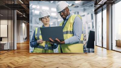 Team of Diverse Professional Heavy Industry Engineers Wearing Safety Uniform and Hard Hats Working on Laptop Computer. African American Technician and Female Worker Talking on a Meeting in a Factory. Wall mural