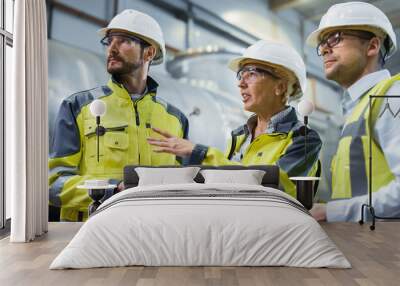 Three Heavy Industry Engineers Stand in Pipe Manufacturing Factory, Use Digital Tablet Computer, Have Discussion. Large Pipe Assembled. Design and Construction of Oil, Gas and Fuels Transport Pipeline Wall mural