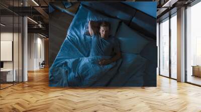 Top View of Handsome Young Man Sleeping Cozily on a Bed in His Bedroom at Night. Blue Nightly Colors with Cold Weak Lamppost Light Shining Through the Window. Wall mural