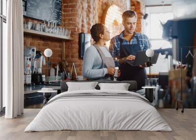 Two Diverse Entrepreneurs Have a Team Meeting in Their Stylish Coffee Shop. Barista and Cafe Owner Discuss Work Schedule and Menu on Laptop Computer. Multiethnic Female and Male Restaurant Employees. Wall mural