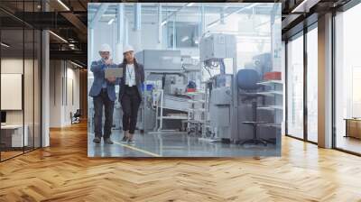 Two Diverse Heavy Industry Engineers in Hard Hats Walking with Laptop Computer and Talking in a Factory. Footage of Two Manufacturing Employees at Work. Wall mural