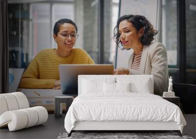 Two Diverse Multiethnic Female Have a Discussion in Meeting Room Behind Glass Walls in an Agency. Creative Director and Project Manager Compare Business Results on Laptop and App Designs in an Office. Wall mural