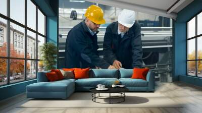 Two engineers discuss a blueprint while checking information on a tablet computer in a factory. Wall mural