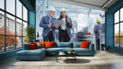 Two Heavy Industry Engineers in Hard Hats Walking with Laptop Computer and Talking in a Factory. Footage of Two Manufacturing Employees at Work in Production Facility. Wall mural