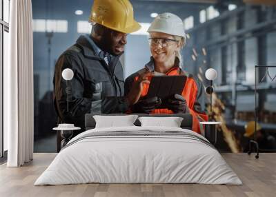 Two Heavy Industry Engineers Stand in Steel Metal Manufacturing Factory, Use Digital Tablet Computer and Have a Discussion. Black African American Industrial Specialist Talk to Female Technician. Wall mural