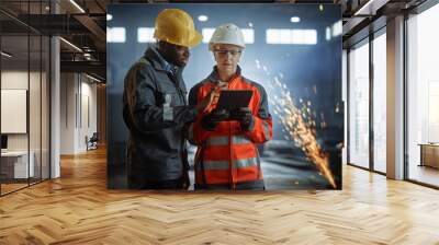 Two Heavy Industry Engineers Stand in Steel Metal Manufacturing Factory, Use Digital Tablet Computer and Have a Discussion. Black African American Industrial Specialist Talk to Female Technician. Wall mural