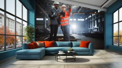 Two Heavy Industry Engineers Stand in Steel Metal Manufacturing Factory, Use Digital Tablet Computer and Have a Discussion. Black African American Industrial Specialist Talk to Female Technician. Wall mural