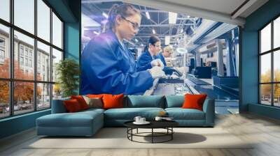 Woman Electronics Factory Worker in Blue Work Coat and Protective Glasses is Assembling Laptop's Motherboard with a Screwdriver. High Tech Factory Facility with Multiple Employees.  Wall mural