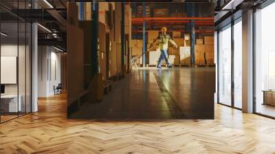 Worker Moves Cardboard Boxes using Hand Pallet Truck, Walking between Rows of Shelves with Goods in Retail Warehouse. People Work in Product Distribution Logistics Center. Side View Shot Wall mural