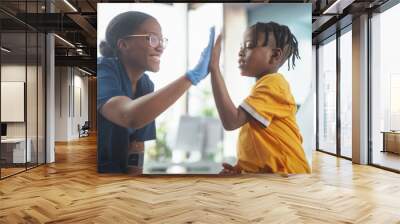 Young African American Boy Sitting In The Chair In Bright Hospital And Getting His Flu Vaccine. Female Black Nurse Is Finished Performing Injection. Professional Woman High-Fives A Kid For Being Brave Wall mural