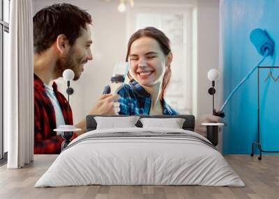 Young Beautiful Couple Decorate Their New Apartment and Fool Around. Husband and Wife are Painting the Wall with Rollers that are Dipped in Light Blue Paint. They are Happy and Have Fun. Wall mural