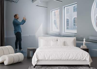 Young Hipster Man in Glasses Standing in Empty Office and Map it with an Augmented Reality Software on a Tablet. Sunlight Shines Through Big Windows. Wall mural