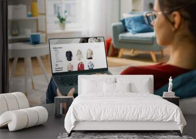 Young Woman at Home Using Laptop Computer for Browsing Through Online Retail Shopping Site. She's Sitting On a Couch in His Cozy Living Room. Over the Shoulder Camera Shot Wall mural