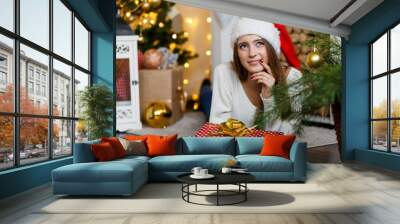 A happy cheerful girl in a redchristmas hat with a gift celebrating new year  Wall mural