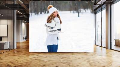 Young girl in warm clothes with ice skates on her shoulder, on a background of winter city park, ice rink. Winter holidays concept. Wall mural