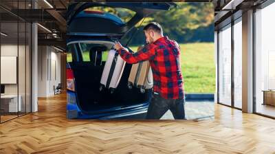 Young man unloads luggage out of the SUV after coming back home from summer family vacation. Wall mural