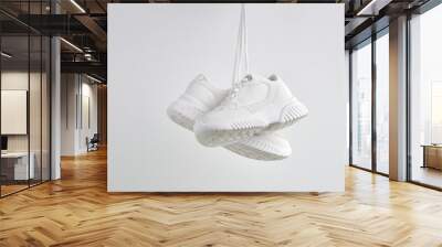 Pair of classic sneakers or trainers hanging on white wall. Casual lifestyle. Fashionable sports shoes. Creative minimalistic layout with footwear mock up for your design. Advertising for shoe store Wall mural