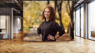 Portrait of cheerful caucasian woman wearing sports clothes and standing in the autumn park Wall mural