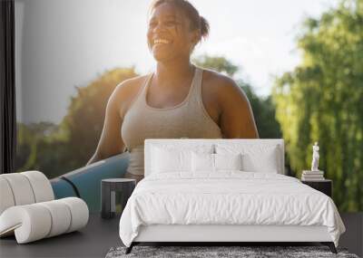 Young African American woman walking with exercise mat and bottle of water through the park in a summer day Wall mural