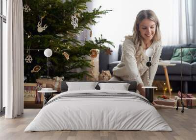 Young caucasian woman putting Christmas gifts under Christmas tree Wall mural