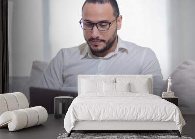 Joven latino trabaja online con su laptop desde la comodidad de su sofá, navegando en internet, y viendo noticias en portales digitales Wall mural