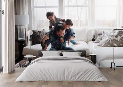 Playful, bonding and father with children on the sofa for playing, quality time and crazy fun. Love, happy and boy kids piling onto their dad with energy on the couch of their family home together Wall mural