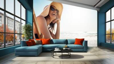 Beach, summer and mockup with a woman laughing while sitting on a chair by the ocean or sea on vacation. Blue sky, view and horizon over water with an attractive young female tourist feeling happy Wall mural