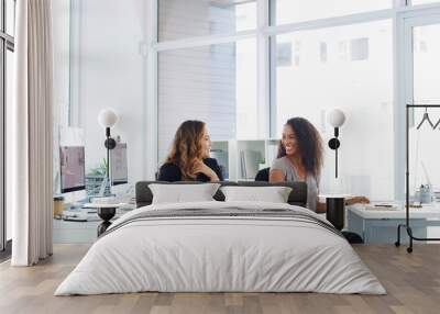 Successful business thrives on teamwork. two young businesswomen chatting at their desks in a modern office. Wall mural