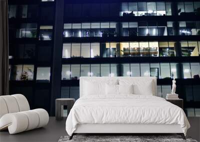 Fragment of the glass facade of a modern corporate building at night. Modern glass office  in city. Big glowing windows in modern office buildings at night, in rows of windows light shines.  Wall mural