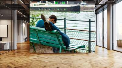 A close up image of a man sitting on a bench with his  lover lying on his lap .Mysterious girl is out of the frame and we only see the feet over the top of the bench.  Wall mural