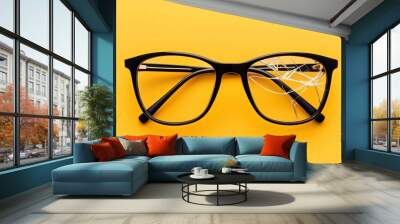 Broken black glasses resting on a bright yellow surface with shattered lens details Wall mural