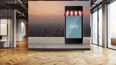 Modern smart mobile phone with online shopping store graphic and open sign on wooden table over blur of cityscape on warm light sundown, Business internet shop online concept Wall mural