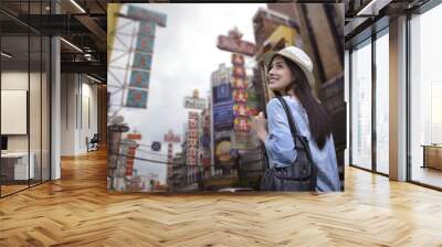 Young asian woman traveler with a backpack on her shoulder and travel hat walking on footpath over China town, Bangkok, Thailand, Travel holiday relaxation concept Wall mural